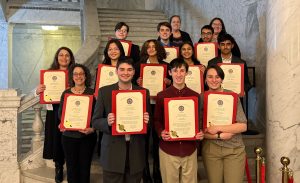 A group of about ten high school and middle school students hold up their certificate of citation at the Maryland State House.