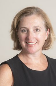 Elizabeth Benton, a white middle-aged woman with blonde hair the ends a little before her chin. She wears a black, sleeveless blouse and smiles.